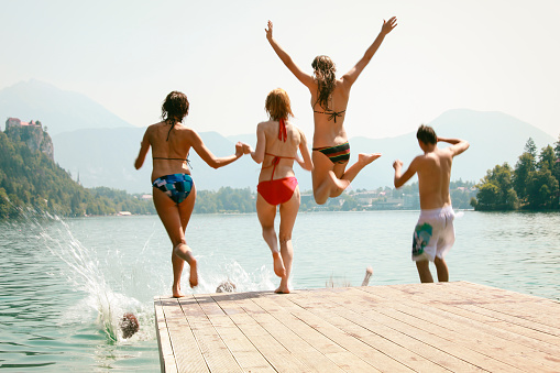 Group of frineds jumping into the lake for a pier. Mid-air, in the water, running, arms in the air...