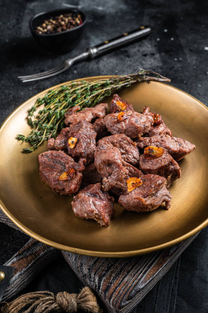 istock Chopped Grilled Diced Beef garlic steak on a plate with thyme. Black background. Top view 1437746342