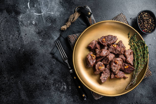 Chopped Grilled Diced Beef garlic steak on a plate with thyme. Black background. Top view. Copy space