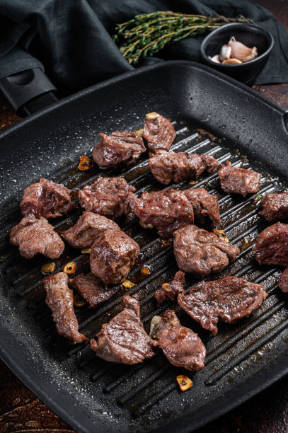 istock Diced beef cubes roasting in a grill pan for stew or goulash. Dark background. Top view 1437746433