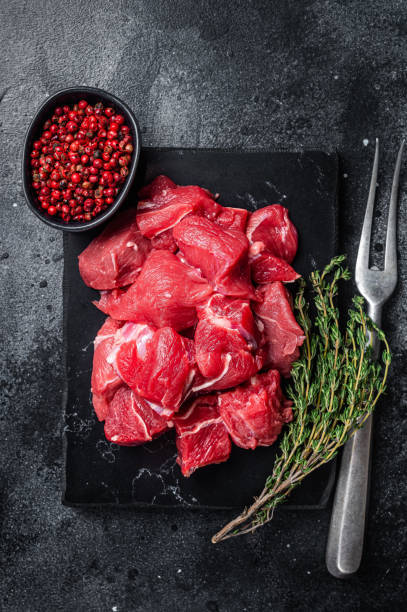istock Raw diced red beef meat for Goulash on marble board. Black background. Top view 1437747076