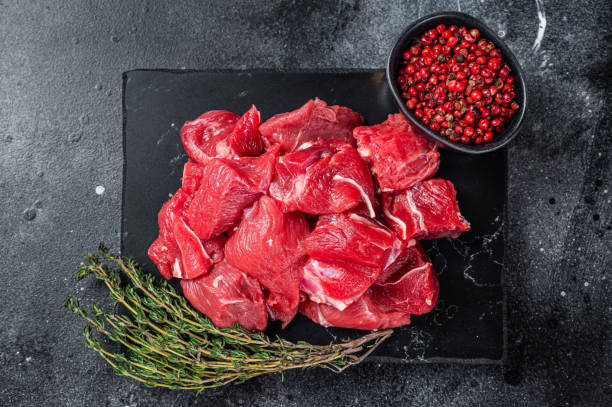 istock Raw diced red beef meat for Goulash on marble board. Black background. Top view 1437747579