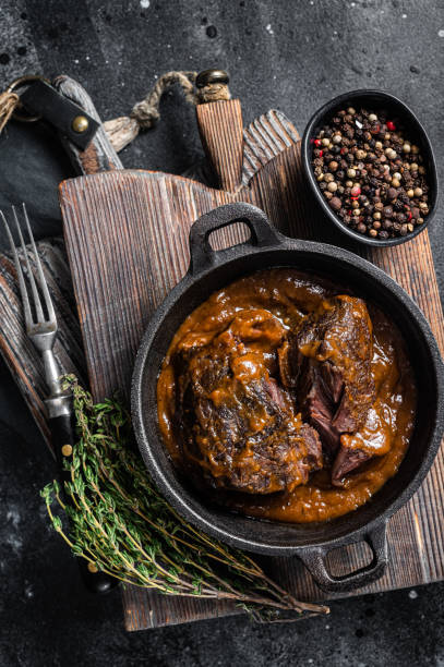 istock Stewed beef cheeks with brown red wine sauce in skillet. Black background. Top view 1437747831