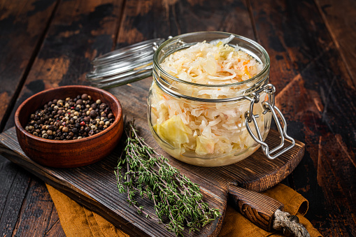 Glass jar with Homemade sauerkraut, black pepper and thyme. Wooden background. Top view.