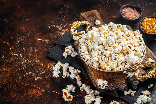 Prepared salty popcorn in a skillet and corn kernel. Dark background. Top view. Copy space.