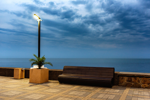 A bench and a burning lantern on the Adler embankment overlooking the sea. Beautiful curly clouds in the sky.