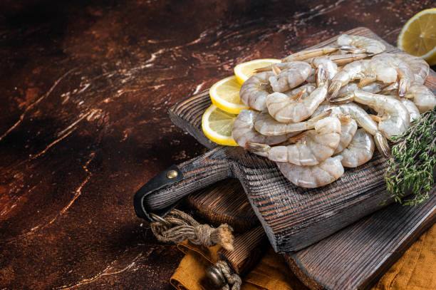 Raw tiger white shrimp prawn on board with herbs. Dark background. Top view. Copy space