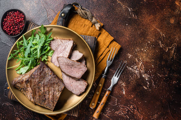 istock Roast Tri Tip or sirloin bottom beef steak on a plate with arugula. Dark background. Top view. Copy space 1437750326