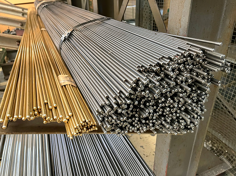 rack full of steel and brass elongated bars, raw material for shafts machining on lathe, rods for series production of small machined turning shafts, horizontal