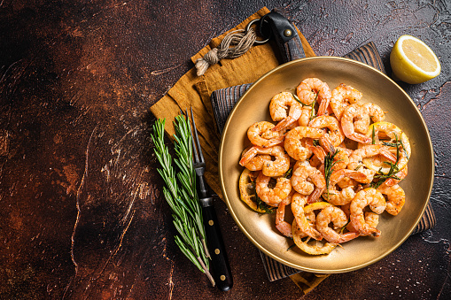 Spicy garlic chilli Prawns Shrimps with lemon and rosemary on a plate. Dark background. Top view. Copy space.