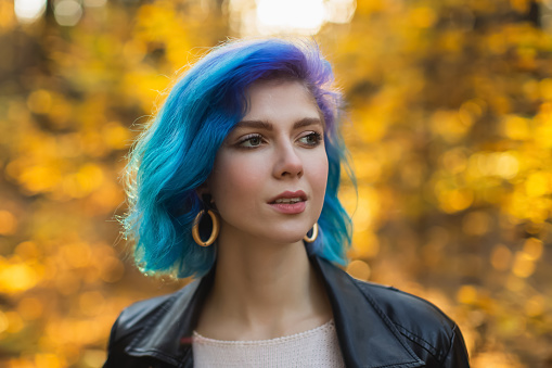 Blue hair woman in jacket in autumn forest. Pretty girl enjoying vacation. Dyed hair