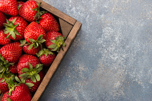 Fresh strawberries in a wood container on the paint background.