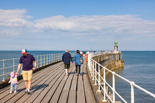 Whitby, UK - September 21, 2022. Man with young child, tourists walking on Whitby Pier, Whitby Harbour