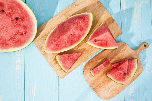 A top view of sliced watermelons on a blue wooden surface under sunlight