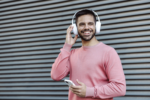A young man holding smart phone and listening music throw his headphones on
