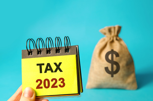 Notes with word Taxes 2023 and money bag. The concept of paying the tax rate. Taxation, taxes burden. Pay off debts. Property income annual taxes