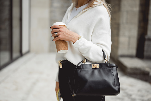 midsection portrait of successful business woman holding cup of hot drink and fashion black bag.