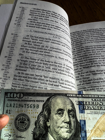 The Holy Bible in English with a tab from the $ 100 banknote showing a passage from the Gospel according to St. Matthew 6:24 You cannot serve God and Mammon