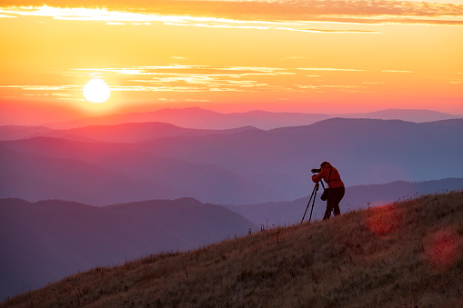 Travel photographer with professional gear makes photos of the amazing sunset high in the mountains