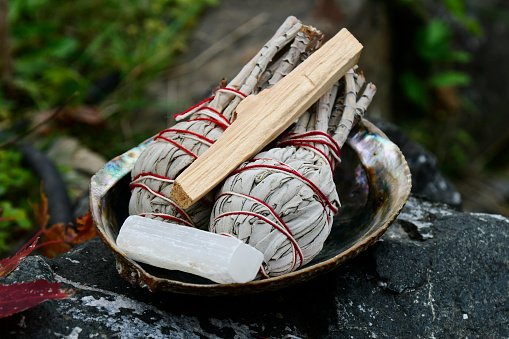 An image of an abalone shell filled with smudge sticks and selenite crystal.