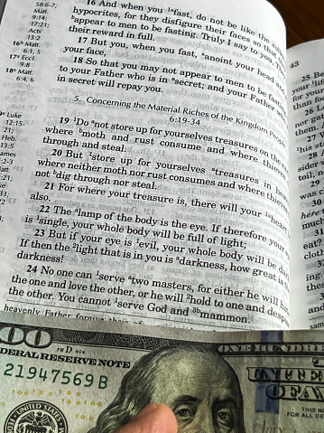 The Holy Bible in English with a tab from the $ 100 banknote showing a passage from the Gospel according to St. Matthew 6:24 You cannot serve God and Mammon