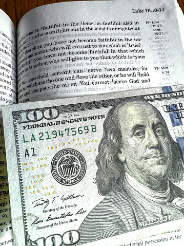 The Holy Bible in English with a tab from the US $ 100 banknote showing the passage from the Gospel according to St. Luke 16.13 You cannot serve God and Mammon