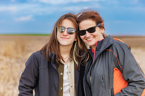 Portrait of teenage girl and her friend standing side by side in agricultural field, wearing sunglasses and smiling, taken on mobile device