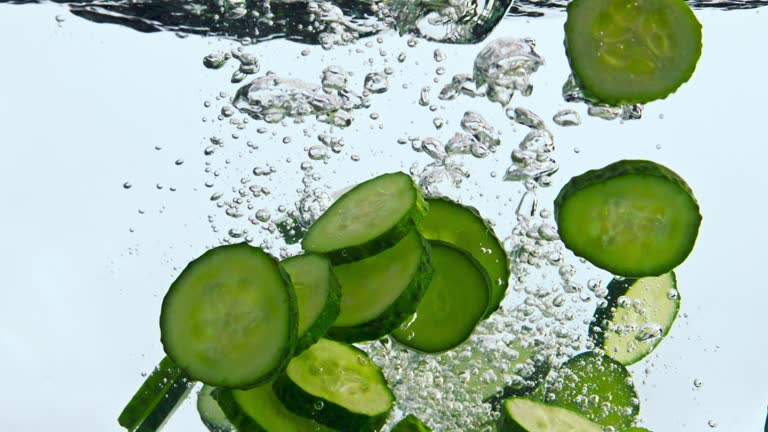 Closeup pieces cucumber dropped in water. Tasty vegetable falling in liquid.