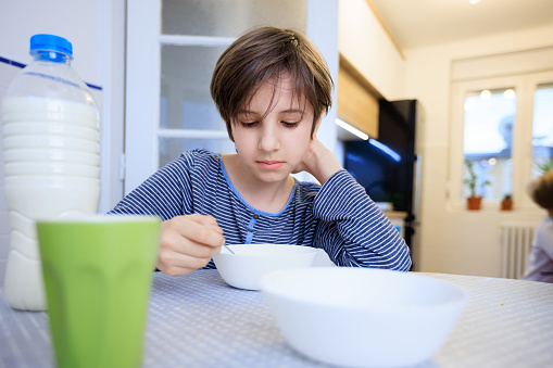 Preadolescent boy sitting at the dining table at home and having breakfast from a bowl, homemade breakfast for healthy lifestyle