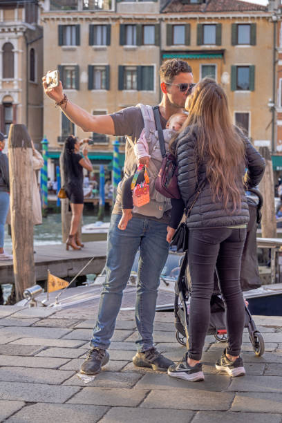 Young coupe taking a selfie while kissing each other Venice, Italy - October 10th 2022: Young couple with a baby having fun kissing each other while taking a selfie in front of the Rialto Bridge in the center of the old and famous Italian city Venice three way kiss stock pictures, royalty-free photos & images