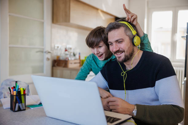 istock Father with headphones using laptop, his son smiling and embracing him from behind 1437776683