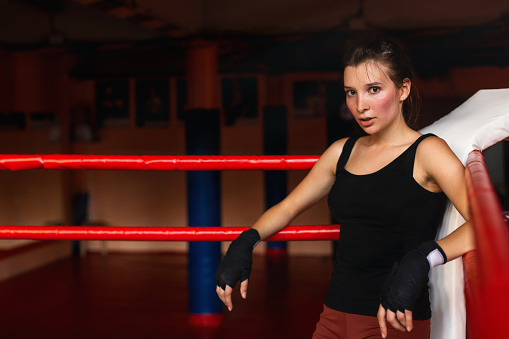 Full length of Caucasian female boxer girl in sportswear stretching on floor in ring.