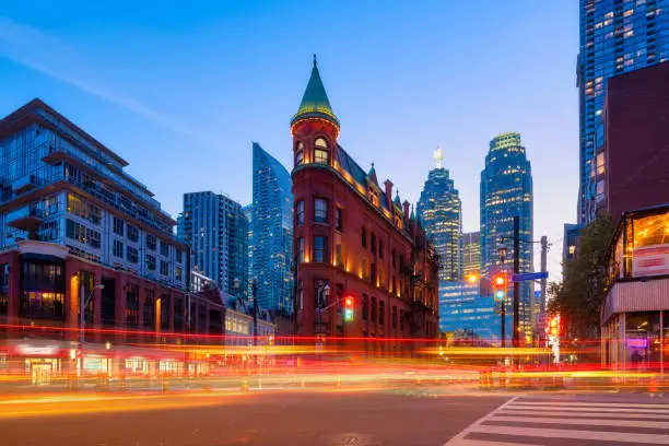 Photo of Canada, Toronto. The famous Gooderham building and the skyscrapers in the background. View of the city in the evening. Blurring traffic lights. Modern and ancient architecture. Night city.