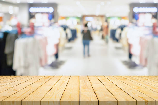 Empty wood table top with blur clothing boutique display interior shopping mall background