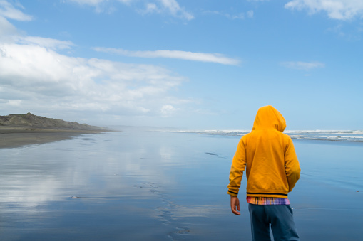 Child wearing hoodies standing on beach of a sea at a clear day.