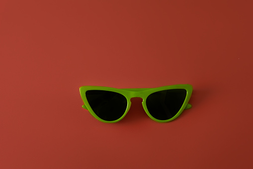 Retro style green sunglasses on red background - travel and vacation concept.
