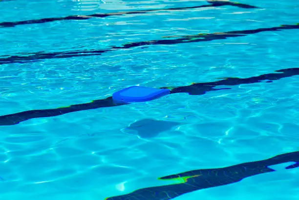 A blue kickboard floats in a swimming pool on a hot, summer day.