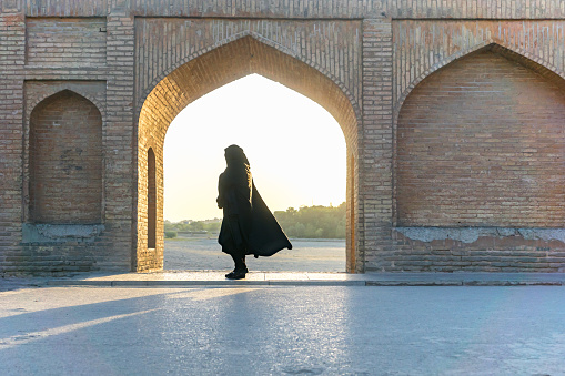 Isfahan, Iran - August 2018: Islamic woman with traditional headscarf and dress on the Khaju bridge in Isfahan, Iran. unidentifiable silhouette like shape of iranian woman in Islamic cloth