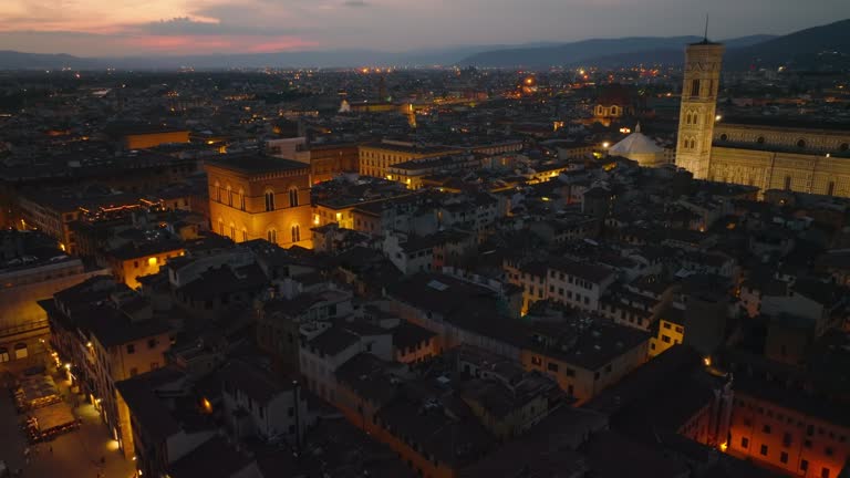 High angle view of buildings in old town, tilt up revealing illuminated famous sights and colour sky at dusk. Florence, Italy