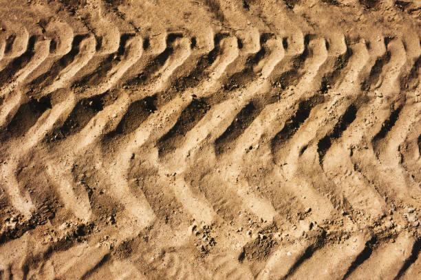 istock Tyre mark background. Tire track shape. Trail lines on dry brown sand pattern. Road construction site backdrop. 1437818904