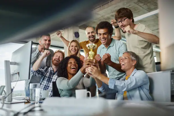 Group of cheerful business colleagues celebrating winning a trophy for their work in the office.