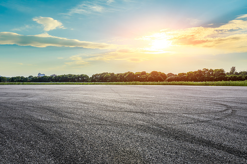 Empty asphalt race track road and green forest with sky clouds at sunset