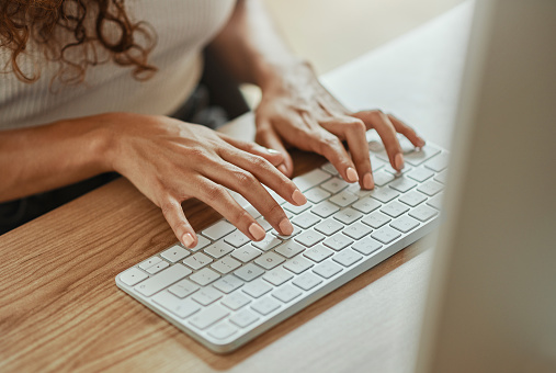 Above, typing and hands of a business woman with a computer for work on the internet at a desk in an office. Corporate employee, worker or receptionist with a keyboard and pc for connection to web