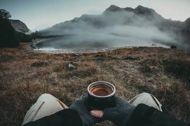 A point-of-view-shot of a person enjoying the natural landscape of mountains with a cup of coffee