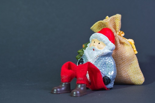 Santa Claus makes a rest sitting leaning on a gift bag, dark background