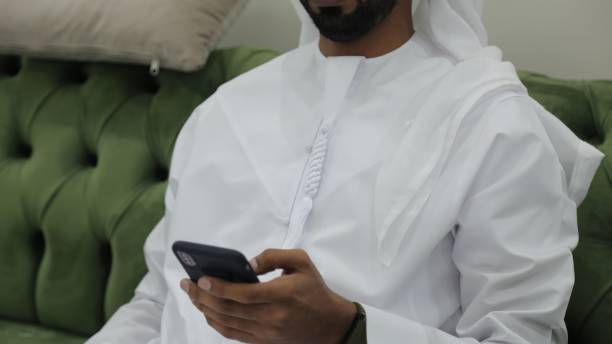 istock Man dressed in a white thobe scrolling through his phone while sitting on a green couch 1437825651