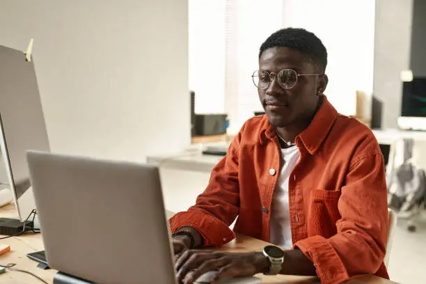 Young African American IT engineer or webdesigner looking at laptop screen while decoding information or creating new website
