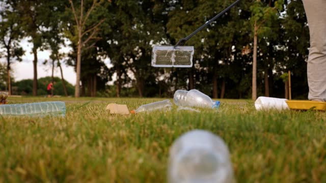 Close-up of a female activist collecting plastic garbage with tongs on the grass