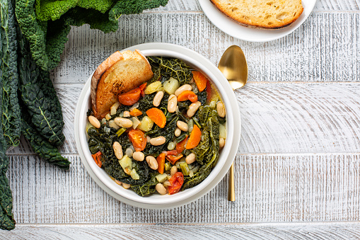 Top view of Ribollita. Tuscan bread soup made with toasted bread and vegetables. Cannellini beans, lacinato kale, cabbage verza, carrot, celery, potatoes, and onion. Itralian food. Directly above.