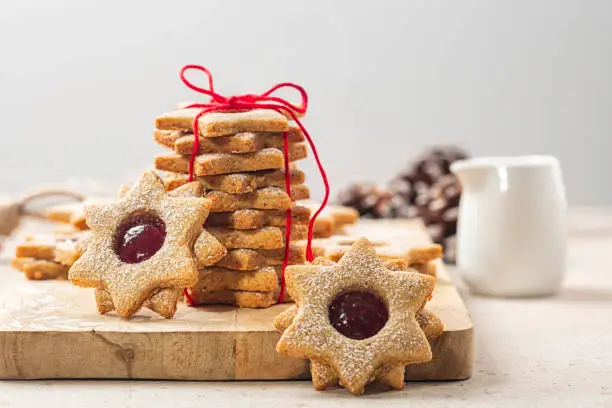 DIY cookie gift. Homemade star or flower shaped linzer cookies with raspberry jam, tied with red ribbon. Christmas or mother day present concept. Selective focus.